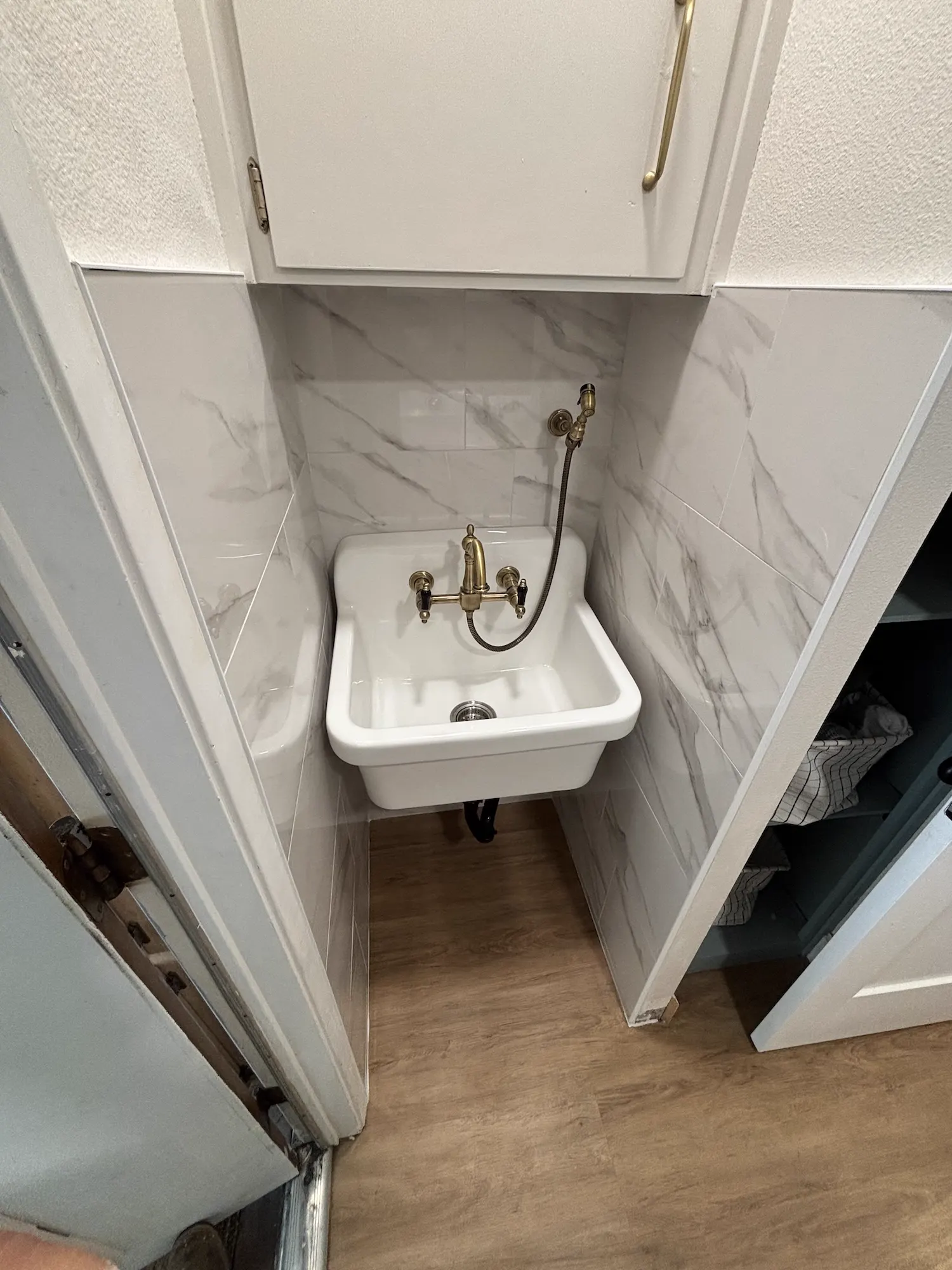 Porcelain wall-mount laundry sink with brass faucet and marble-look tile in Fresno
